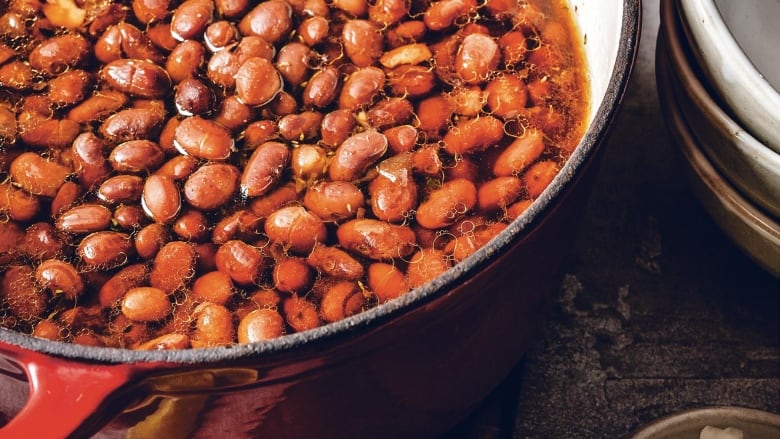 Closeup overhead shot of a red pot of beans next to a stack of bowls. 