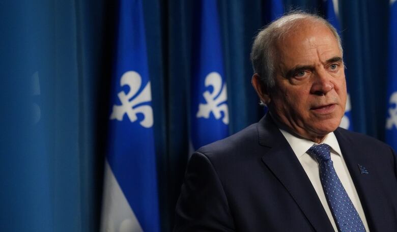 A white middle aged man in a suit in front of Quebec flags