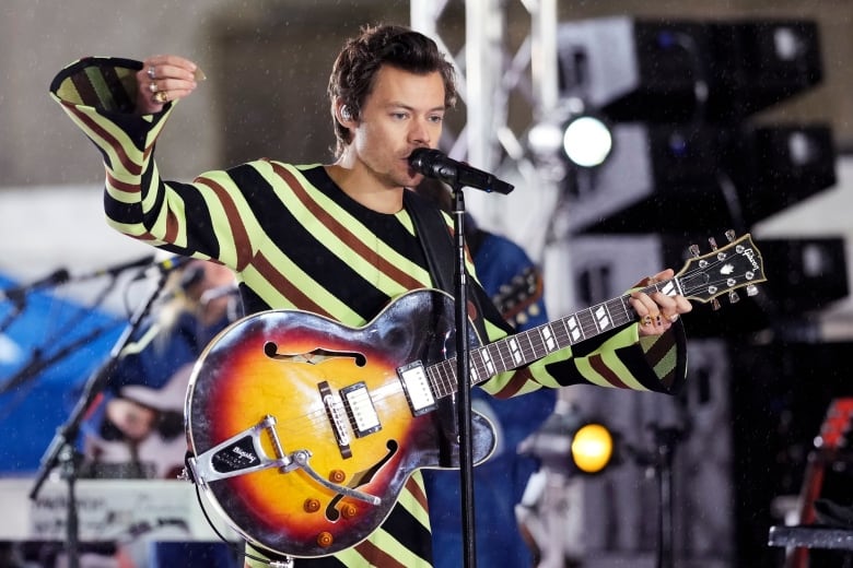 A man holds a guitar and speaks into a microphone. 