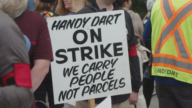 A person at a rally holds a sign that reads 'Handydart on Strike We carry people not parcels'.