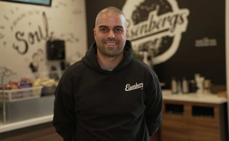 A man stands smiling in a black sweatshirt. 