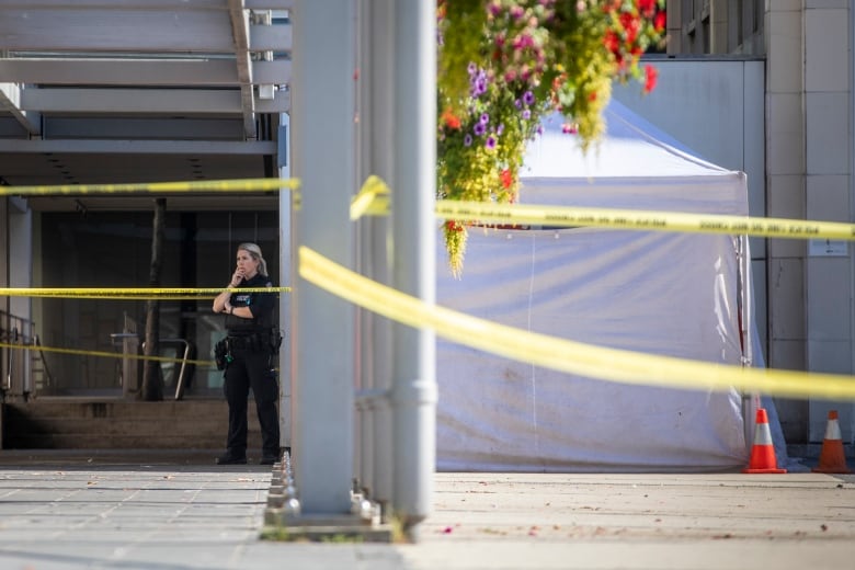 A VPD officer stands next to a white tent and crime scene tape.