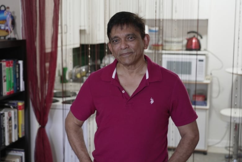 Man standing in his apartment in front of the kitchen.