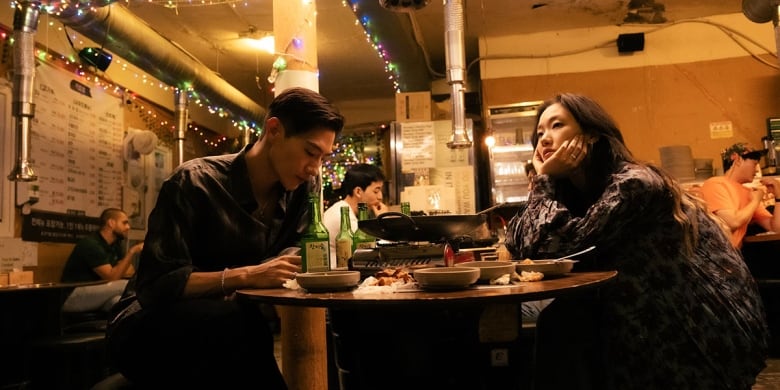 A Korean man and woman sit at a table for a meal in low light.