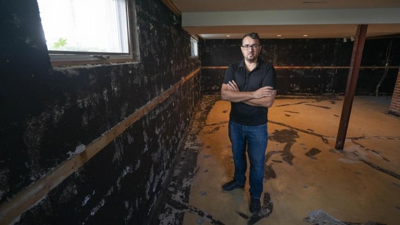 A man is pictured standing in an empty, water-stained basement.