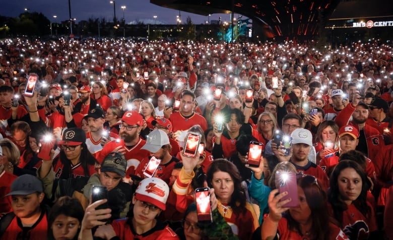 A group of people hold phones in the dark. 