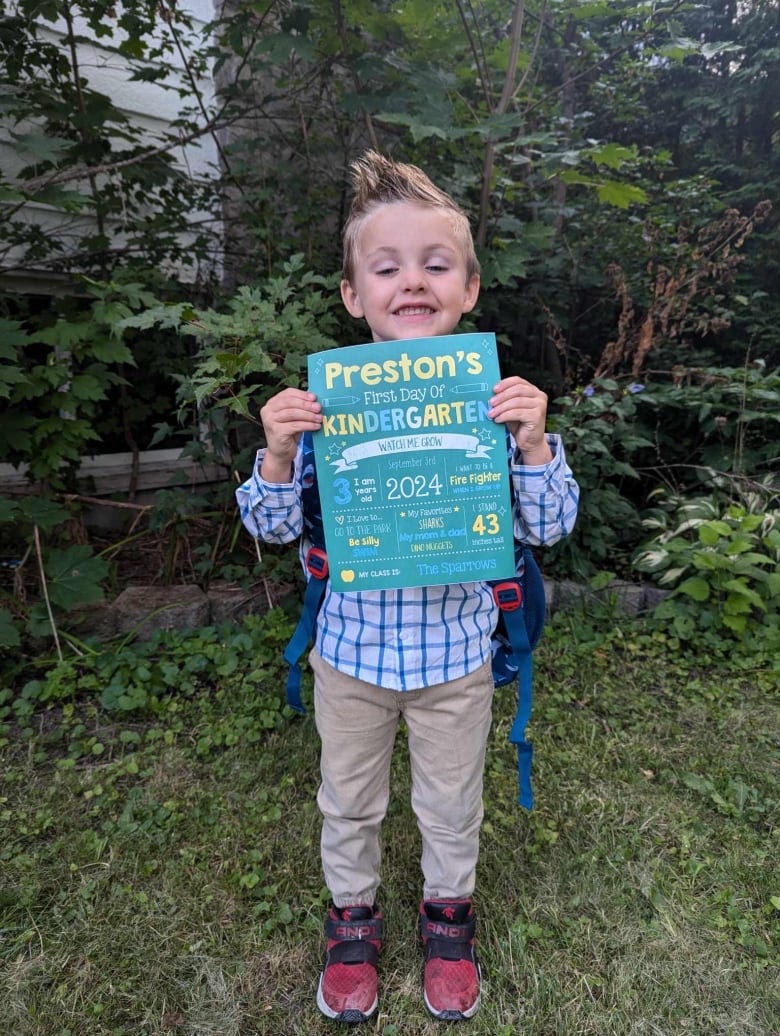 A little smiling boy holds a  sign that says Preston's first  day of Kindergarten