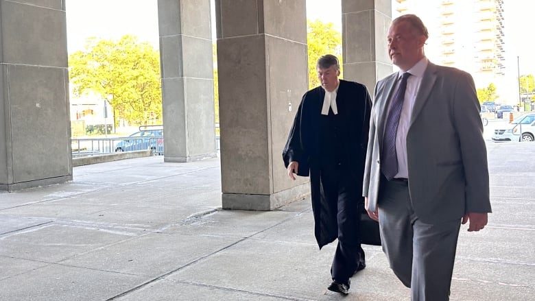 A man in a suit and another wearing legal robes walk into a large building.