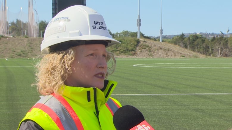 A woman wearing a white, construction hat with City of St. John's written on it and a Hi-Vis safety jacket.