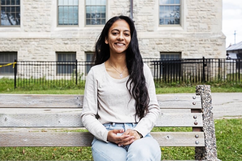 Woman on a sweater sits on a bench smiling