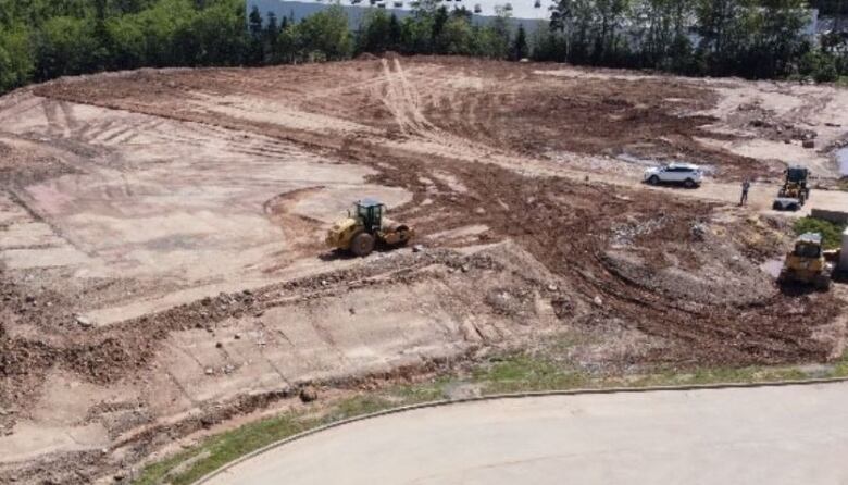 An overhead view shows a lot levelled with brown dirt, surrounded by a ring of trees