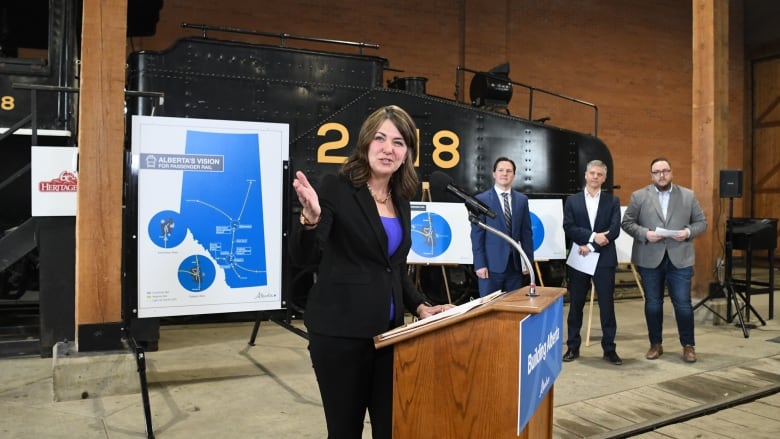 A woman points, standing in front of an old train and three men.