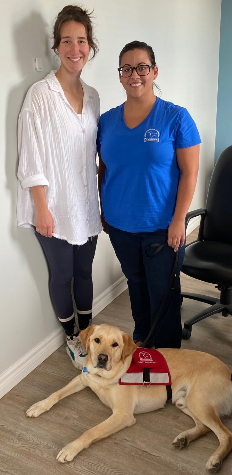 Two women stand next to each other with a dog by their feet.