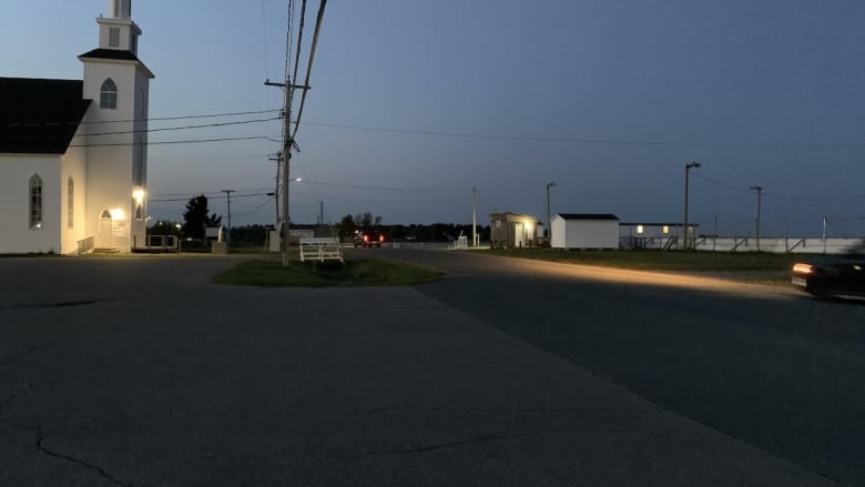 A dark street with a white church on the left.