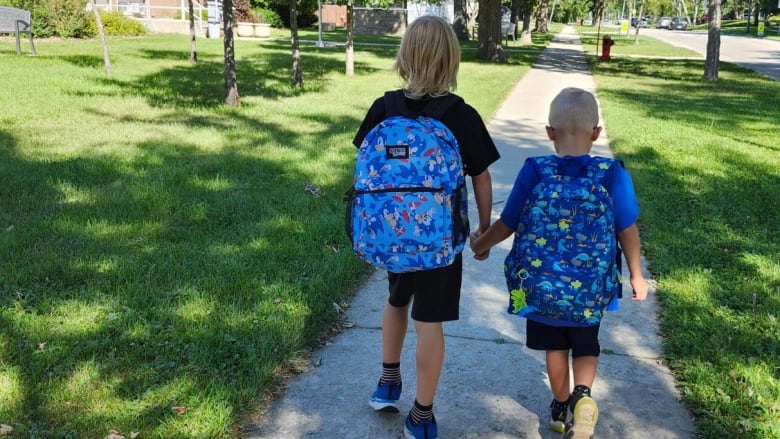 Two young boys are seen from behind walking on a sidewalk