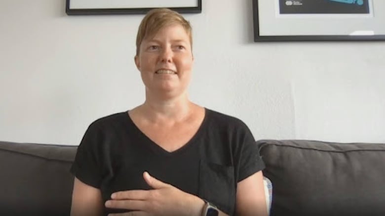 A woman sitting on a couch with a couple of framed posters hanging in the wall.