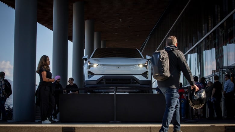 A man is seen walking in front of an electric vehicle. 