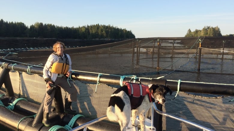 A woman and her dog stand in a playground. The woman is smiling.