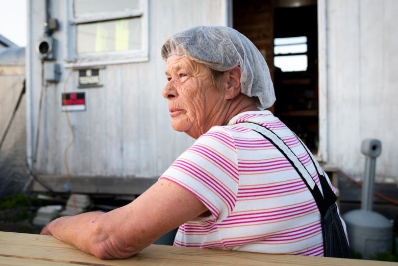 An older woman in a hairnet sits outside at a picnic table, shown in profile.