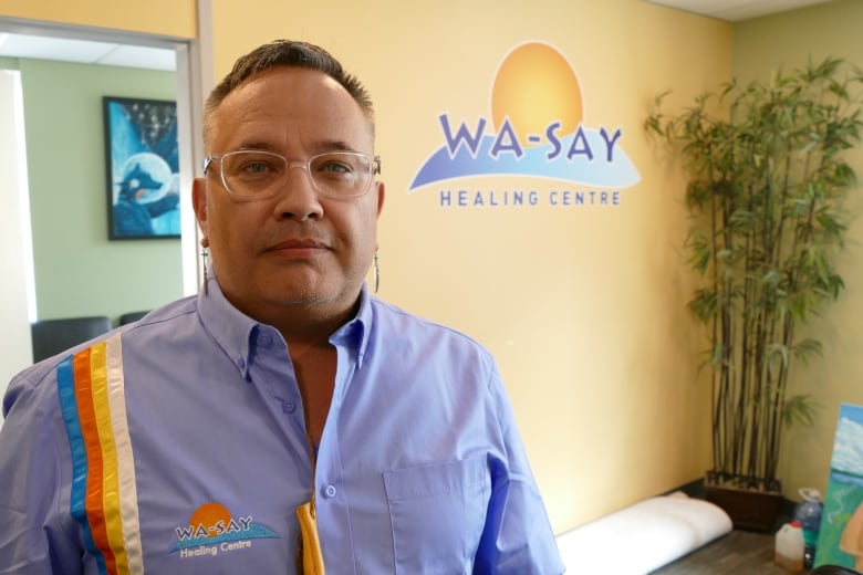 A man standing in front of wall with a logo that says 'Wa-Say Healing Centre'