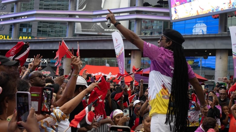 Photo of a man performing to a crowd of several people holding Trinidad and Tobago flags. 