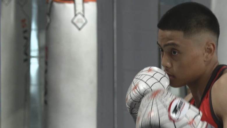 A boy with boxing gloves on takes a fighting stance.