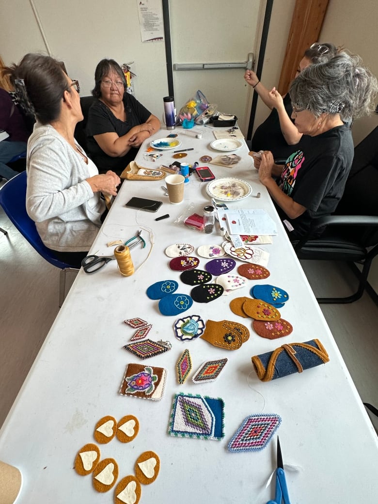 Four women chat while beading at a table.