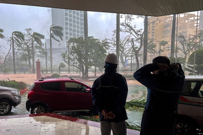 Two people stand outside a building during a typhoon.