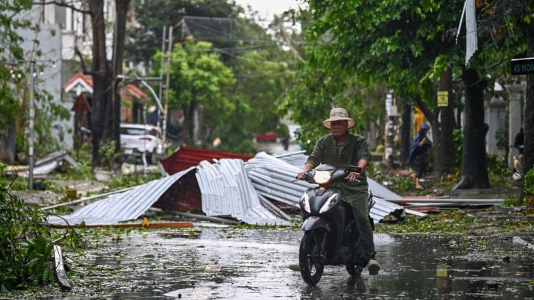 A man rides a scooter past storm debris. 