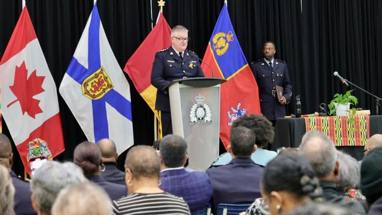 Member of RCMP talks at podium in front of a large crowd of onlookers. 