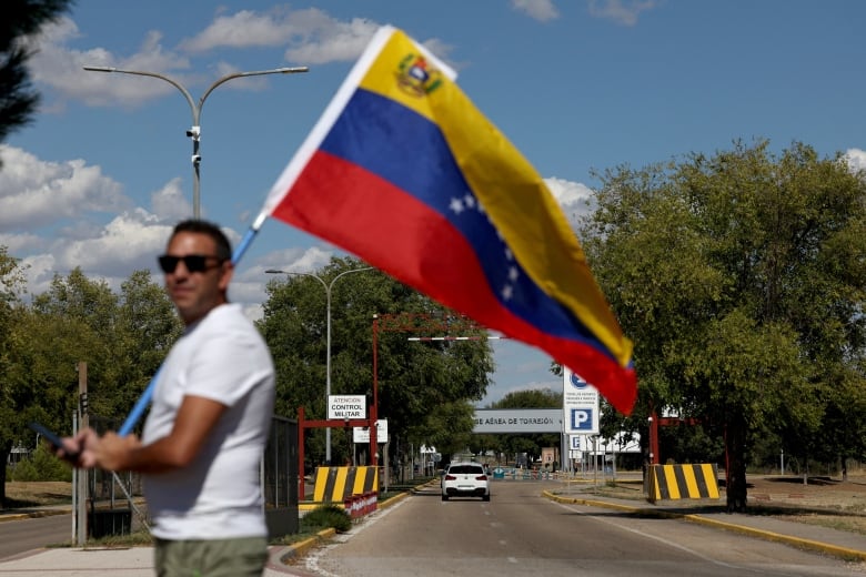 A person holds a flag near a road leading to an airport.