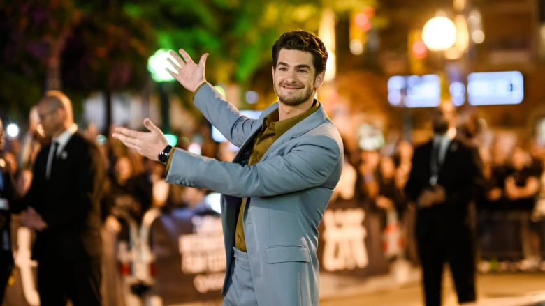 Actor Andrew Garfield arrives for the red carpet of the film We Live in Time, on a street, smiling for the cameras with fans behind a police barrier during TIFF at night.