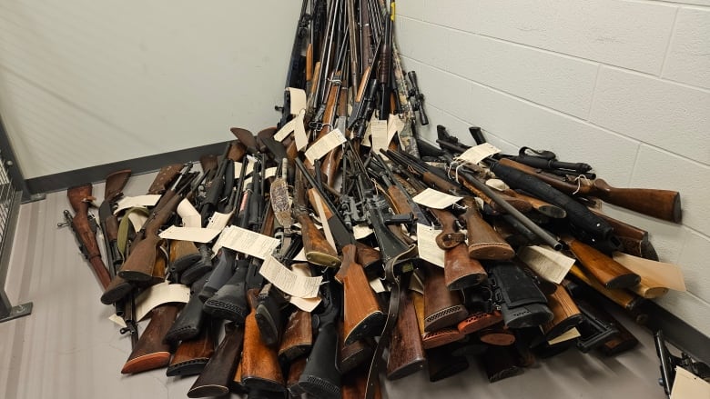 A pile of more than 50 rifles with beige tags on them in a room at a police detachment