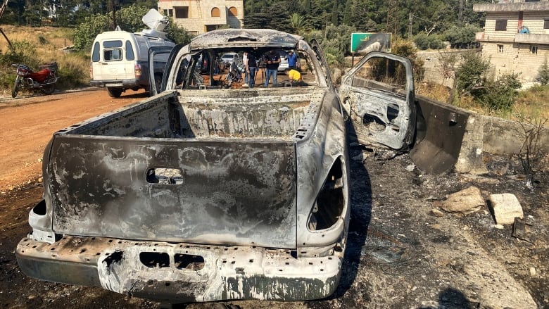 A burned and damaged small truck is shown on a dirt roadway.