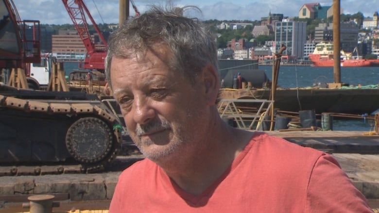 A man wearing an orange t-shirt stands at a small boat basin construction site.