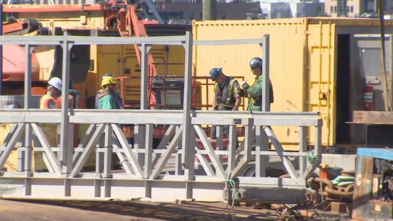 Four construction workers with Hi Vis jacket and hard hats working on a bridge with cranes behind them.