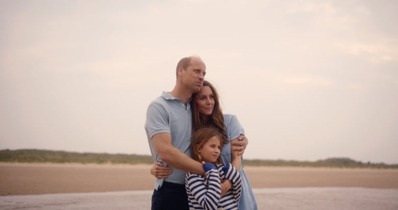 A man, a woman and their young daughter are seen together on a beach. They are all wearing blue.