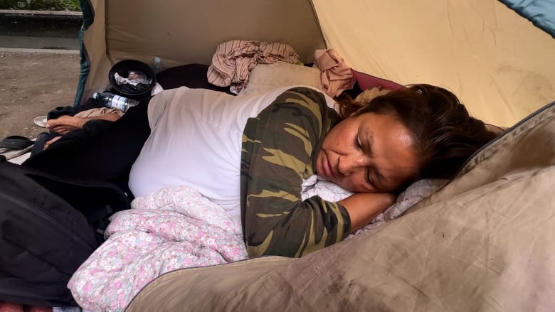 A First Nations woman lies in a tent wrapped in blankets.