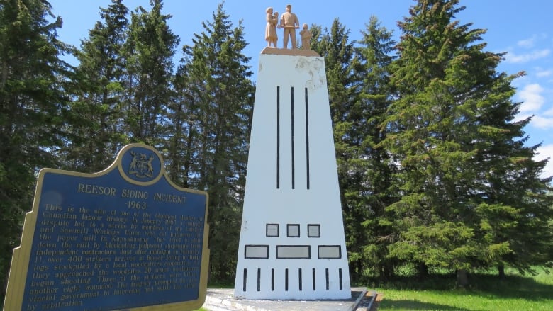 A tall white monument with statues of a family at the top.