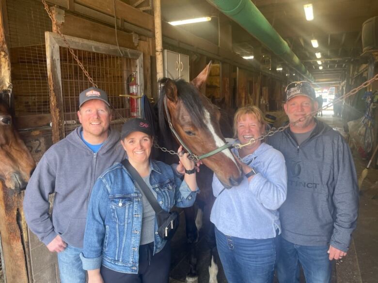 Four people stand with a horse in a barn 