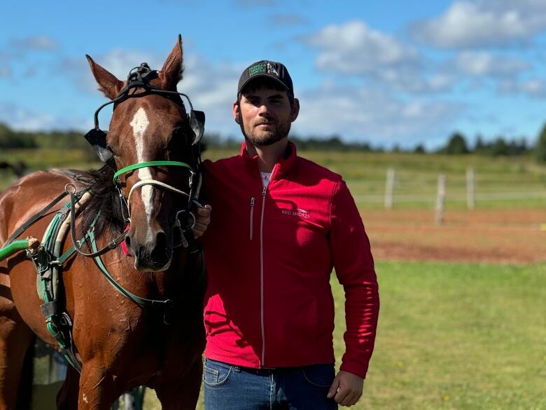 A man in a red sweater stands with a horse on a farm 