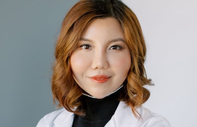 A headshot of a person who is wearing a medical jacket over a turtleneck.