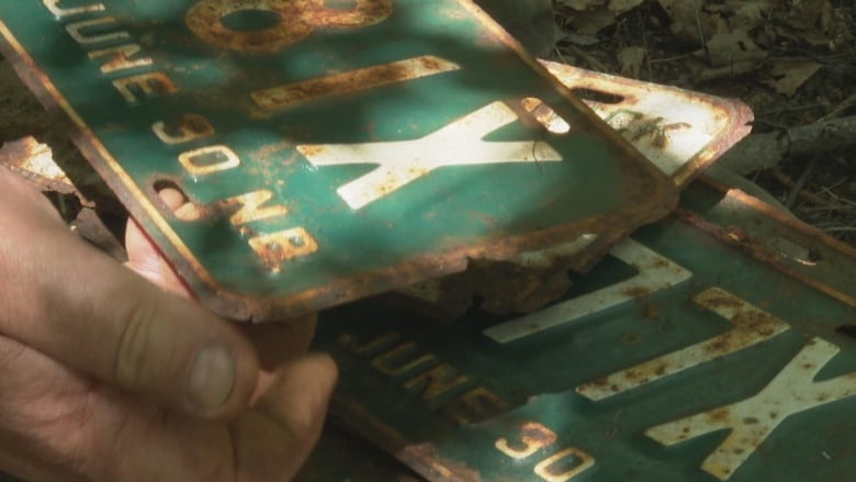 A man's hand is shown holding a rusted green licence plate.