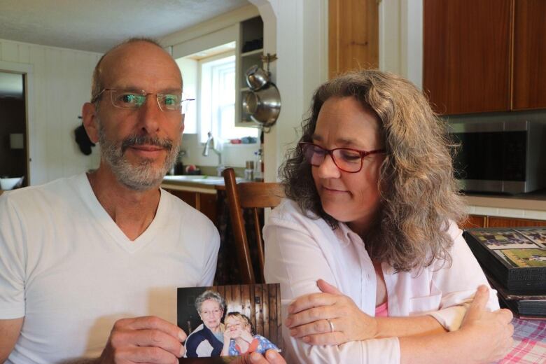 A couple holds a photo of an elderly woman with a child making a silly face 