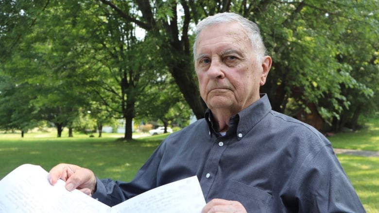 A woman sits outside looking at the camera. In his hands are hand-written notes 