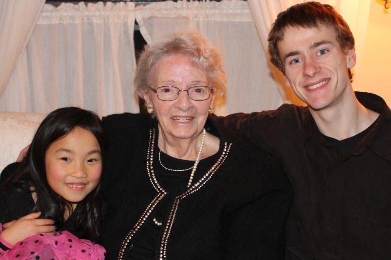 A grandmother smiles at the camera, taking a photo with her grandchildren