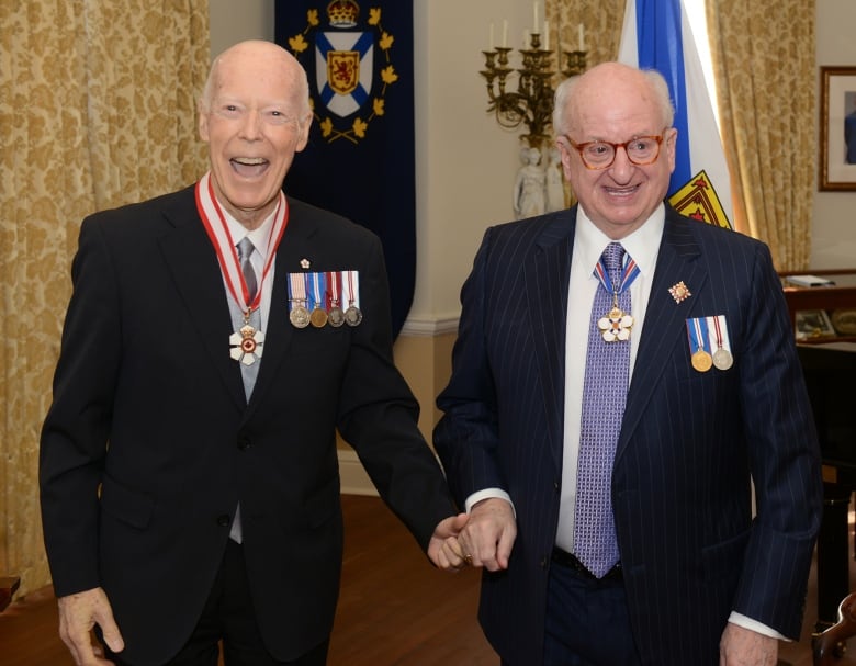 Two men in suits with medals and ribbons pose together for a photo.