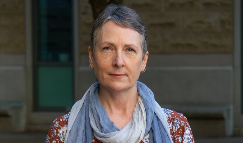 A woman with short grey hair looks to the camera.