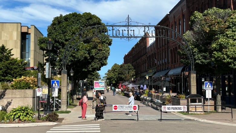 A large grey building is seen at the left, next to a blocked-off street with a big wrought-iron sign reading Victoria Row. Historic buildings line that street. 