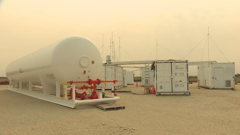 A system with a large white tank sits in a farm field.